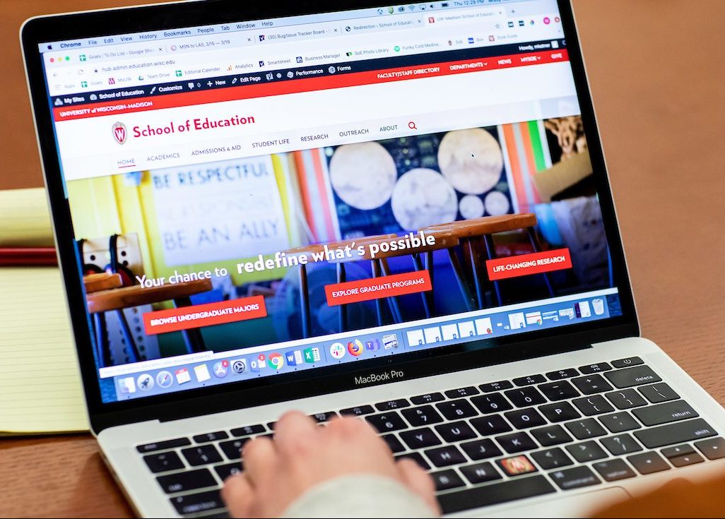person typing on a laptop computer with the school of education homepage screen open