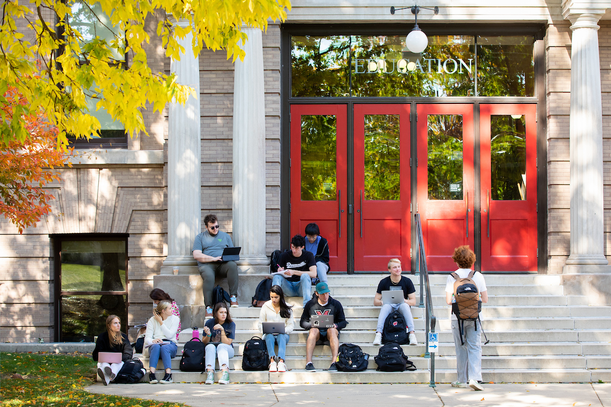 Students study sitting on the steps in front of the Education Building in fall