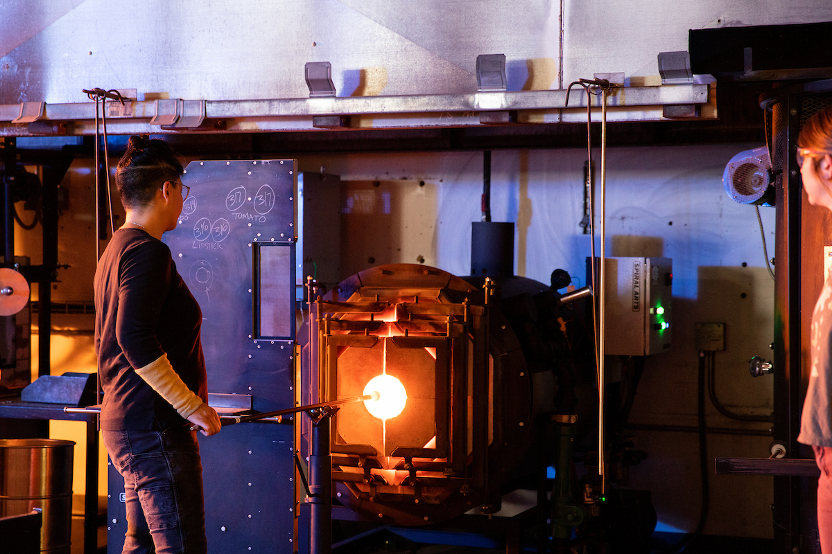 Helen Lee puts glass into a glowing furnace