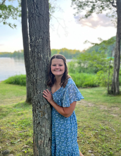 Abigail Laumer in a blue dress leaning on a tree