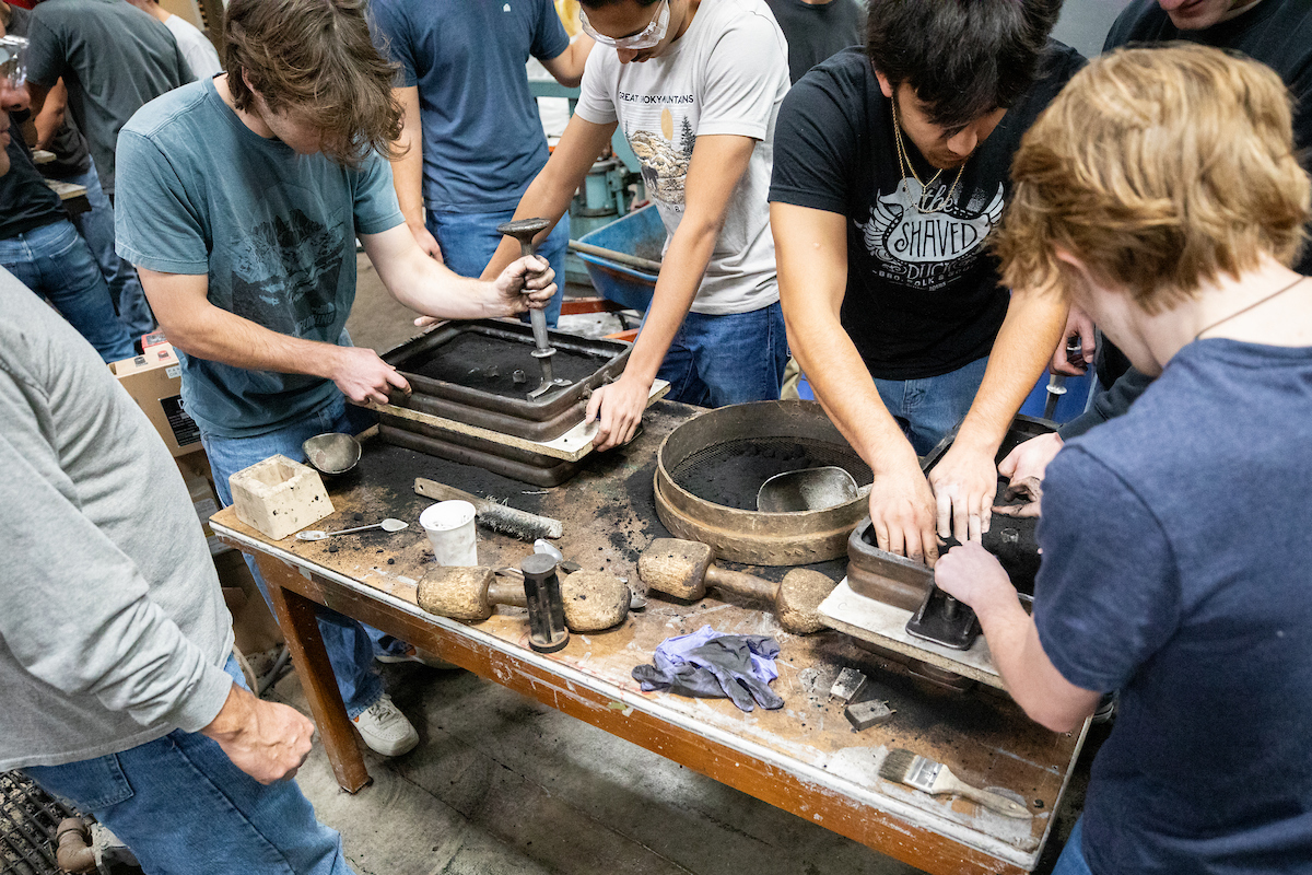 Students compact sand around a model to create the mold cavity for a screwdriver handle