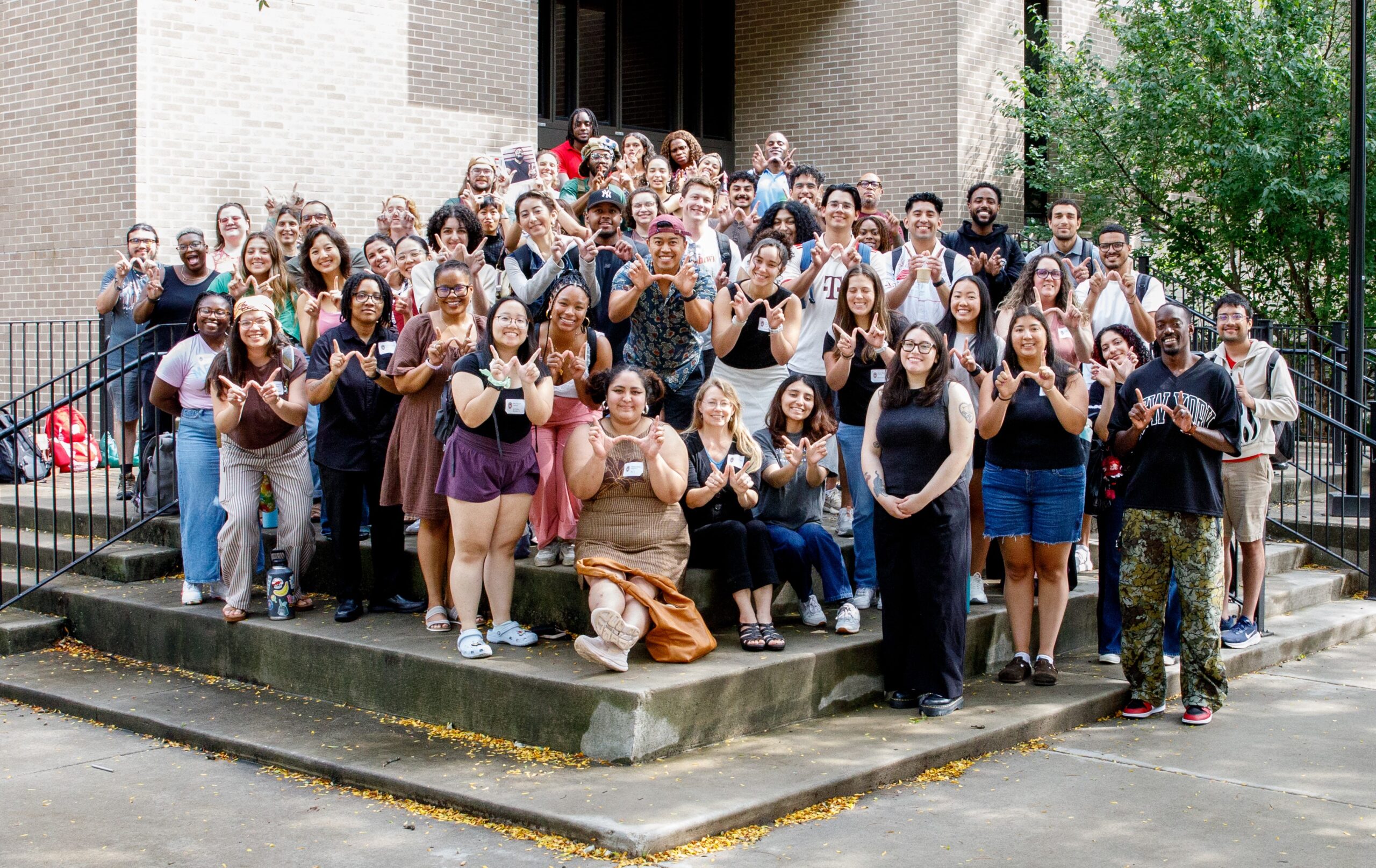 Group photo on outdoor stairs of Teacher Education Building, most students forming a W with their hands.