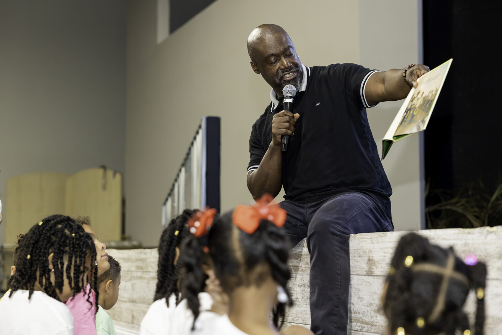 Jerry Jordan reads to children while sitting on a stage.