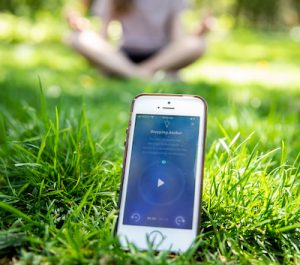 a woman meditates in the grass next to a phone