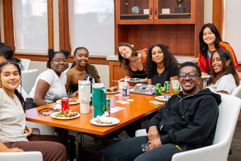 A group of students smiling at a table with food and beverages.