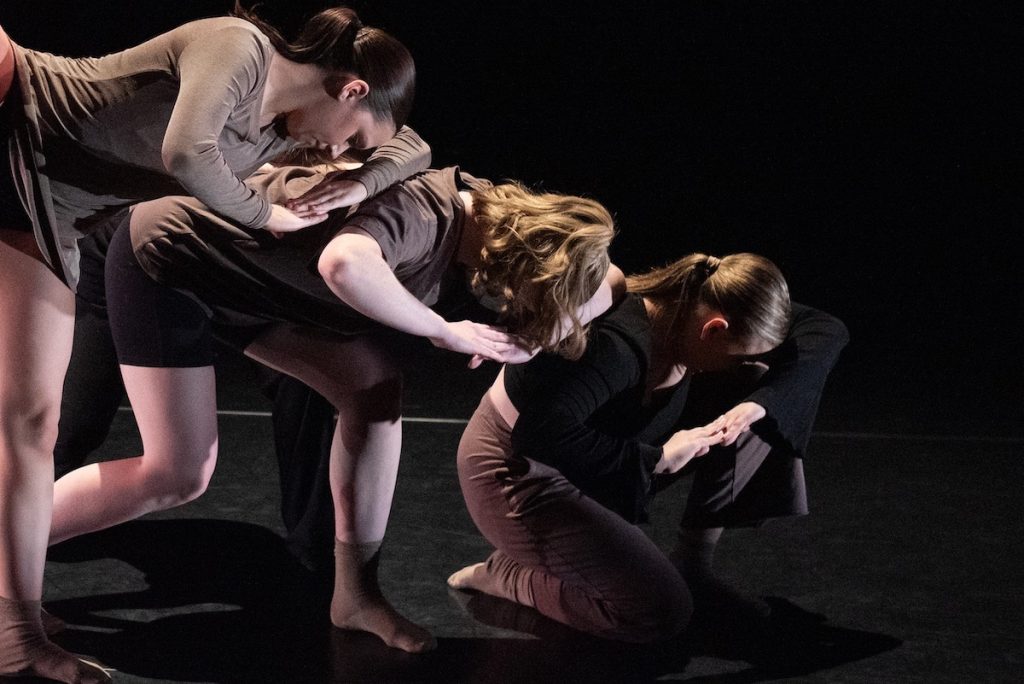 Three student dancers create a shape together during a performance.