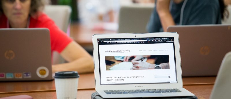 Laptop with a cup of coffee next to it at a table with others on laptops