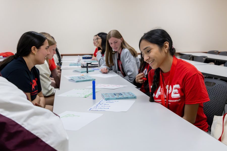 a student smiling while working at a table with other students