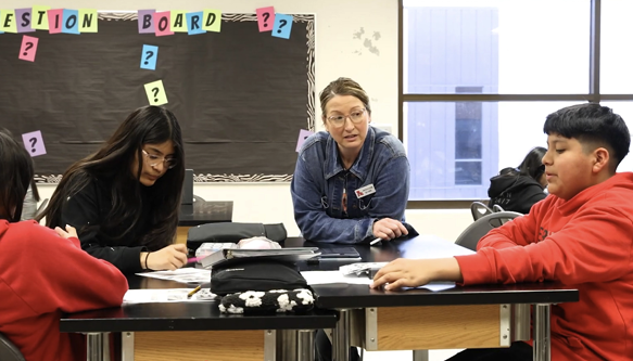 teacher sits at a table with students