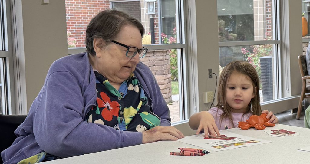 an older women helps a young child color a picture